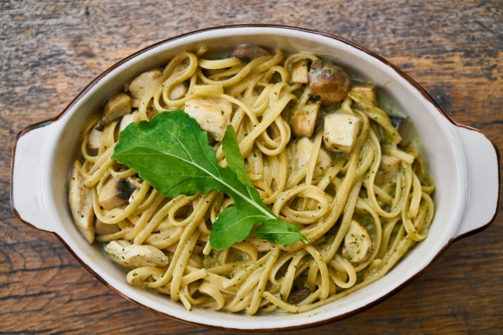 Understanding Carbohydrates for Sports Performance: Bowl of pasta noodles, chicken with a leaf on top.